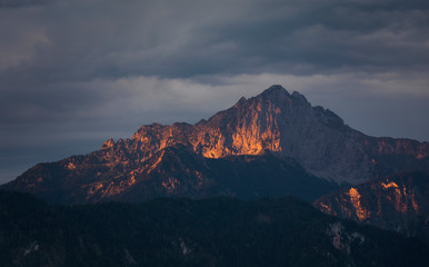 Naklejka premium Sunlight in mountains during sunrise at lake Forggensee, dramatic dark clouds in the sky, Bavaria.