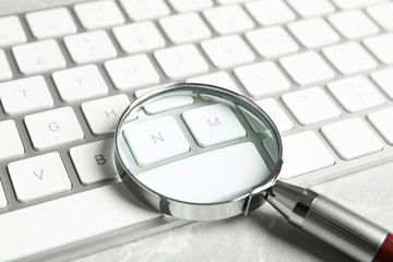 Magnifying glass and computer keyboard on light grey marble table, closeup. Search concept
