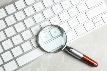 Magnifying glass and computer keyboard on light grey marble table, top view. Search concept