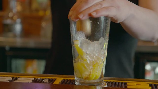 Bartender making a cocktail crushing ice over lemon and limes in glass