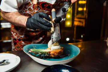 The cook rubs the cheese on a grater over the cooked salad.