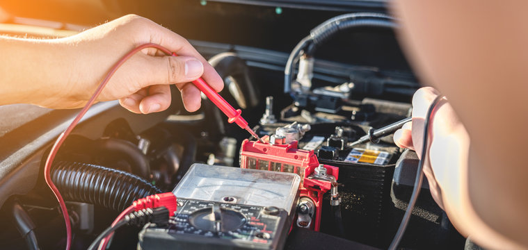 Mechanic repairman checking engine automotive in auto repair service and using digital multimeter testing battery to measure various values and analyze, Service and Maintenance car battery check