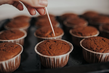 Chocolate muffins bakery. Brownie cupcakes on the baking pan. Baking at home, home bakery. Woman cheсks muffins with toothpick.