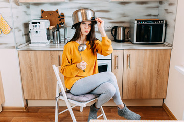 Home duties while quarantine and self-isolation. Young woman is cooking in the kitchen while quarantine. Woman with saucepan on head and ladle in hand.