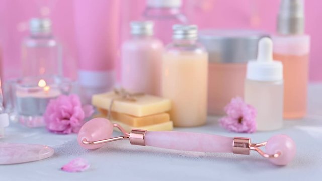 pink rose quartz roller lies on white sink edge against blurry beauty acids and facial serum close zoom out