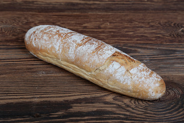 Crunchy, oblong freshly baked bread sprinkled with flour, top view. A fresh, loaf of bread lying on brown, wooden boards.