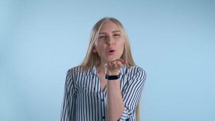 Young lady sending an air kiss and blinking with one eye on blue background. She is pretty and smiling woman.