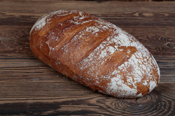 Crunchy, freshly baked bread sprinkled with white flour. View of a fresh, well-baked, brown loaf on wooden boards.