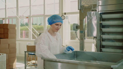 Candy factory. Factory worker checking packing machine. Young woman in uniform inspecting packing machine while working in confectionery factory.
