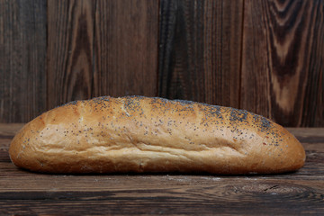 Crunchy, freshly baked bread sprinkled with poppy seeds. Side view of a fresh, loaf of bread on brown, wooden boards.
