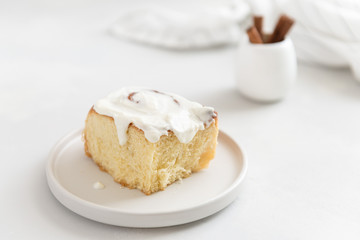 Freshly baked cinnabon or cinnamon roll with creamcheese frosting on gray plate white background. Side view, close up. Bakery menu, recipe, cook book. Hygge
