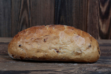 Side view of a crunchy, delicious, freshly baked bread on a wooden, rustic table. In the background brown boards.