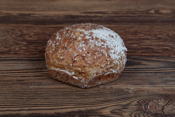 Top view of a fresh, dark, hexagonal bread sprinkled with flour. Loaf on a rustic, wooden table with brown boards.