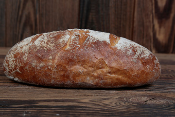 Side view of fresh, crusty bread sprinkled with flour. A freshly baked brown loaf on a wooden rustic table. In the background brown boards.
