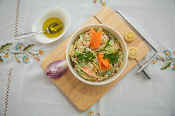 Chopped red onion . olives on a small white bowl . wooden board . Salad with ham, red and orange pepper, mushrooms, pickles, white sauce, on a white bowl and olives.
