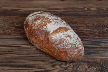 View of fresh, crusty bread sprinkled with flour. A freshly baked, golden, brown loaf on a wooden, rustic table.