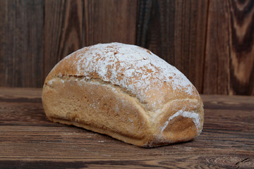 View of fresh, crunchy mold bread sprinkled with flour. A freshly baked, rectangular loaf on a wooden, brown, rustic table. In the background brown boards.