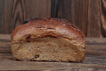 Side view of fresh, crunchy, dark bread stuffed with dried fruit with cracked crust. A freshly baked loaf on a wooden, brown, rustic table.