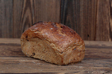 Fresh, stuffed, molded bread with cracked crust. A freshly baked loaf on a wooden, brown, rustic table. In the background brown boards.