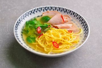 Japanese ramen soup with noodles, beef, egg, fresh parsley and sweet pepper on gray background. Copy space banner.