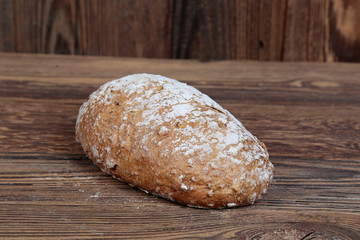 View of fresh bread sprinkled with flour. A freshly baked, golden loaf on a wooden, brown, rustic table. In the background brown boards.