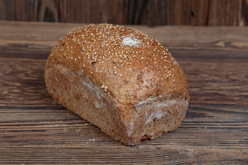 View of fresh bread sprinkled with sesame seeds. A freshly baked molded, golden loaf on a wooden, brown, rustic table. In the background brown boards.