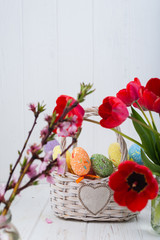 Multi-colored Easter eggs in a basket on a white wooden background