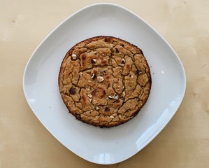 Chickpea banana and peanut butter cake with toasted nuts - above view with  geometric setting. cake in a white square plate with light wood background