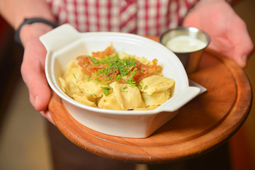 Waiter holds a plate of tasty Italian food Ravioli. Italian cuisine in restaurant, Ravioli dumplings with meat and sauce