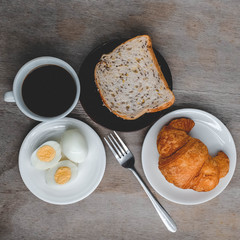 Croissant on white plate on wooden table, Breakfast served with black coffee. Balanced diet.
