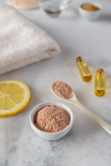 Ceramic bowl with red clay powder, ingredients for homemade facial and body mask or scrub and fresh sprig of flowering cherry on white background. Spa and bodycare concept.