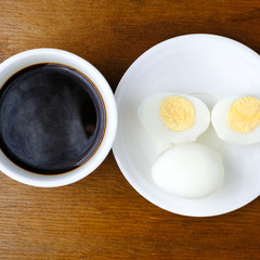 halves of boiled eggs on white plate and black coffee on wooden rustic background. the view from the top