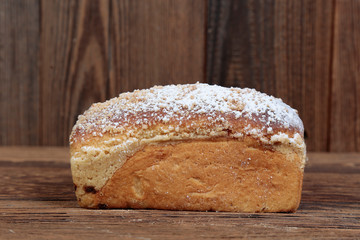 Side view of fresh, crunchy mold bread sprinkled with flour. A freshly baked, rectangular loaf on a wooden, brown, rustic table. In the background brown boards.
