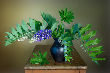 Still life with beautiful purple lupines in a vase on a table on a brown background