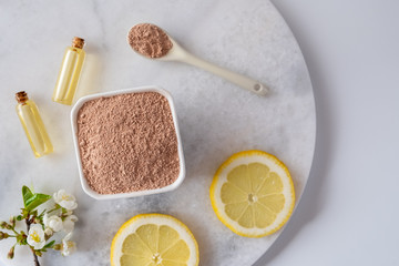 Ceramic bowl with red clay powder, ingredients for homemade facial and body mask or scrub and fresh sprig of flowering cherry on white background. Spa and bodycare concept.