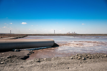 stream of muddy water runs out from drain pipe into slurry pond of dressing factory