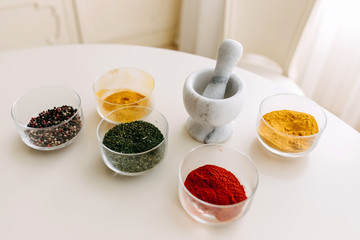 White stone mortar and glass bowls with spices: turmeric, curry, mix of pepper and herbs.