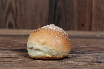 Side view, close-up of a fresh, homemade bread roll with sprinkles on a wooden, brown, rustic table.
