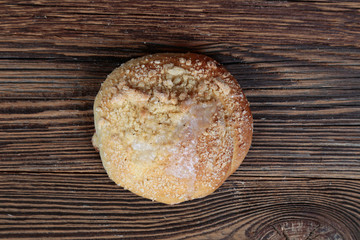 Top view, close-up of a fresh, round, homemade, bread roll with sprinkles on a wooden, brown, rustic table.
