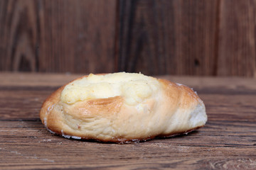 Side view, close-up of a fresh, homemade bun with filling on a wooden, brown, rustic table.