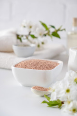 Obraz na płótnie Canvas Ceramic bowl with red clay powder, ingredients for homemade facial and body mask or scrub and fresh sprig of flowering cherry on white background. Spa and bodycare concept.