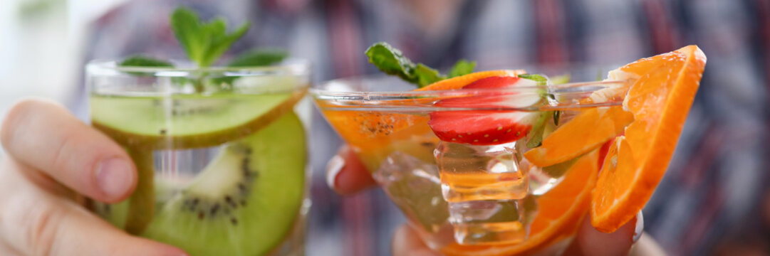 Close-up of male and female hands holding two different bright cocktails with fresh fruits. Glasses with delicious alcoholic drinks. Holiday and celebration concept