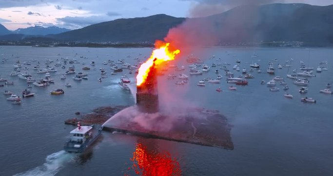 Unbelievably beautiful, cinematic, low level, close flying by, aerial drone footage that reveals the biggest bonfire event on Earth and small boats gathering around it near Alesund, Norway at dusk.