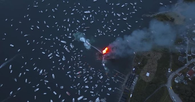 Unique revealing, high altitude, top down drone footage of small motor boats and sail boats gathering around and witnessing the biggest bonfire event on Earth at Alesund, Norway at dusk.