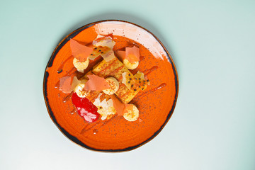 Banana pancake or crepe, with maple syrup and powdered sugar served on a orange brown plate over blue mint background.