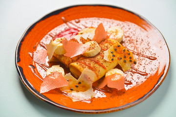 Banana pancake or crepe, with maple syrup and powdered sugar served on a orange brown plate over blue mint background.