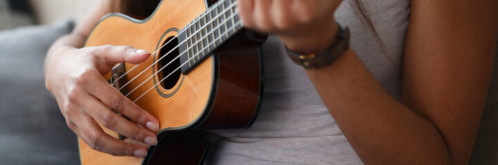 Obraz premium Close-up of latino woman holding ukulele and learning how to play. Young female exercising in playing. Musical wooden instrument. Music and art concept