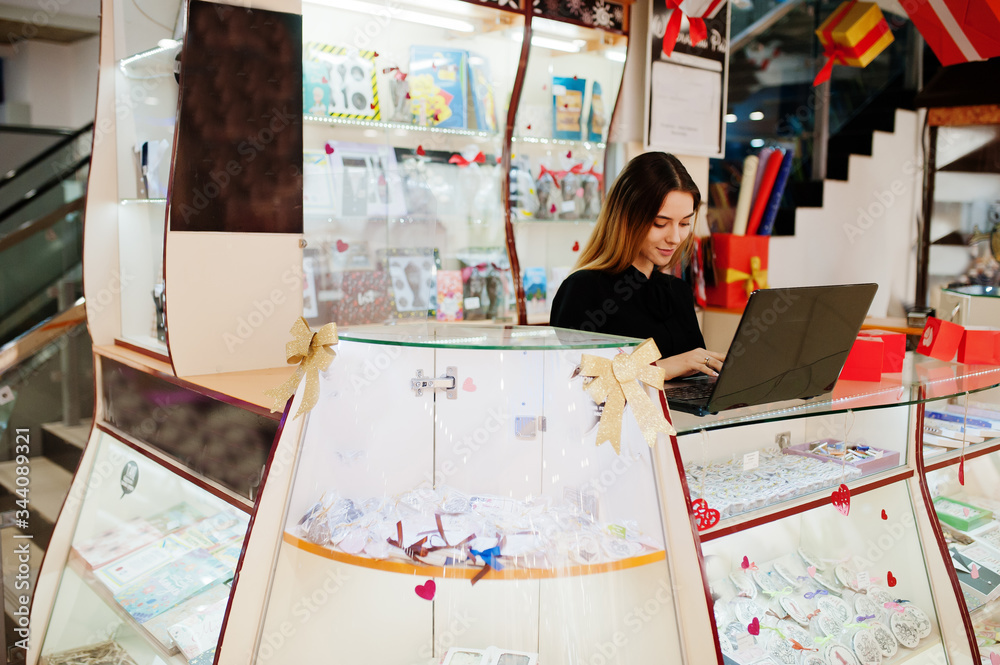 Wall mural Portrait of young caucasian female woman seller using laptop. Small business of candy souvenirs shop.