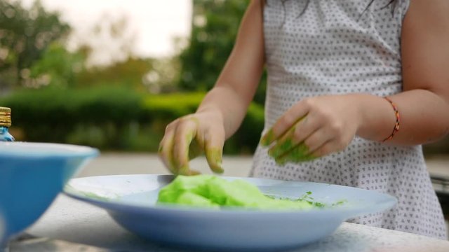 Asian young child girl is making Thai dumplings dessert or Bualoy sweets. Child preparing green glutinous rice dough and make Bualoy balls into bowl before boiled with coconut milk and sugar.