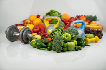 Fitness concept. Healthy nutrition: fruits and vegetables. Equipment for fitness exercises: weighing machine and dumbells. White background.